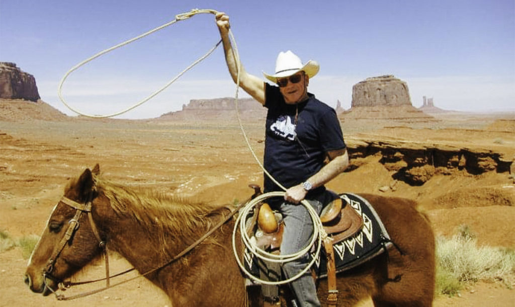 Robert Beleson on horseback spinning a rope lasso over his head in the desert