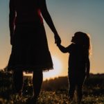 Silhouettes of a mother and child walking in a field at sunset