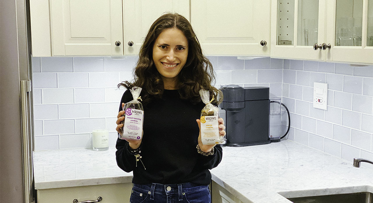 2015 Birthright Israel alumna Morgan Spindler in her kitchen holding up two packages of cookies from Morganic Bakeshop