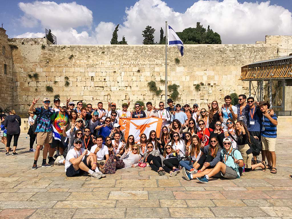 2015 Birthright Israel alumnus Ethan Frank with is group in front of the Kotel holding the University of Texas Longhorns flag