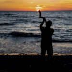 A man blowing a shofar at the sea.